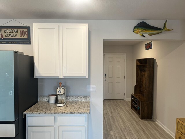 kitchen with light stone countertops, white cabinets, light hardwood / wood-style floors, and fridge