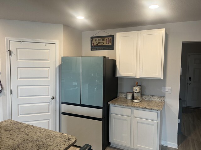 kitchen with light stone countertops, white cabinetry, dark hardwood / wood-style floors, and stainless steel refrigerator