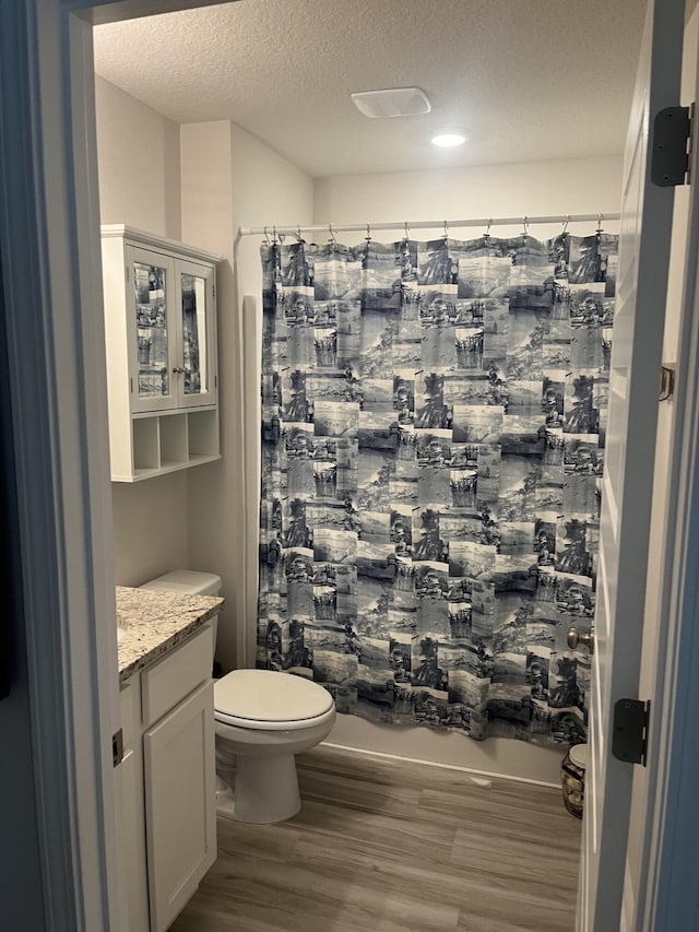 full bathroom featuring a textured ceiling, shower / tub combo, hardwood / wood-style floors, vanity, and toilet