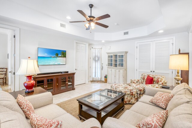 living room with light tile patterned flooring, ceiling fan, crown molding, and a tray ceiling