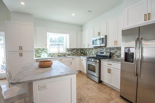 kitchen featuring appliances with stainless steel finishes, light stone counters, white cabinets, a kitchen island, and sink