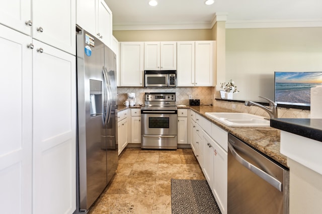 kitchen with sink, white cabinets, appliances with stainless steel finishes, crown molding, and dark stone countertops