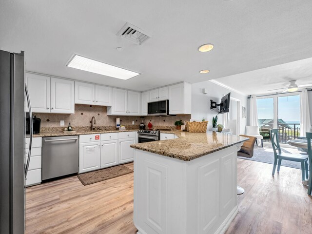 kitchen with appliances with stainless steel finishes, light hardwood / wood-style floors, white cabinets, kitchen peninsula, and a skylight