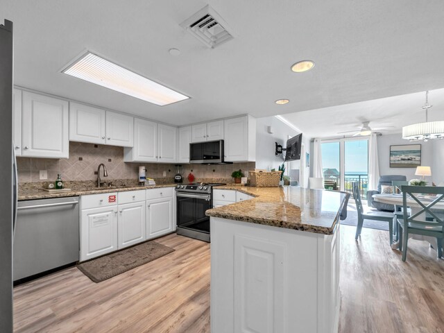 kitchen featuring white cabinets, kitchen peninsula, hanging light fixtures, light hardwood / wood-style flooring, and stainless steel appliances