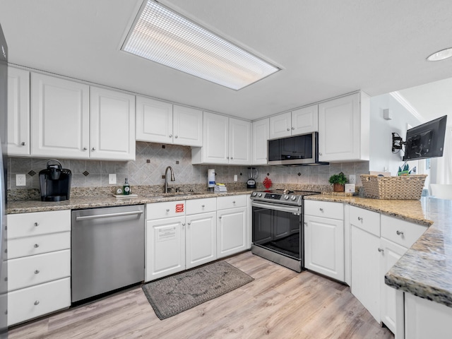 kitchen featuring sink, tasteful backsplash, white cabinetry, stainless steel appliances, and light wood-type flooring