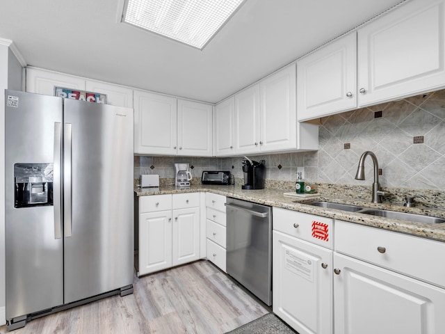 kitchen featuring appliances with stainless steel finishes, decorative backsplash, light hardwood / wood-style floors, white cabinets, and sink