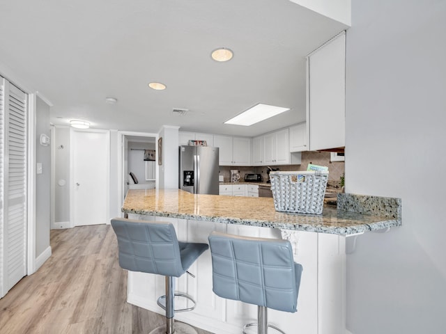 kitchen with a breakfast bar area, white cabinetry, kitchen peninsula, light hardwood / wood-style flooring, and stainless steel fridge