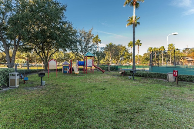 view of play area featuring tennis court and a yard