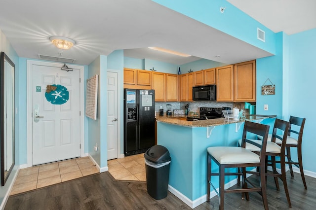 kitchen featuring kitchen peninsula, a kitchen bar, backsplash, black appliances, and light hardwood / wood-style flooring