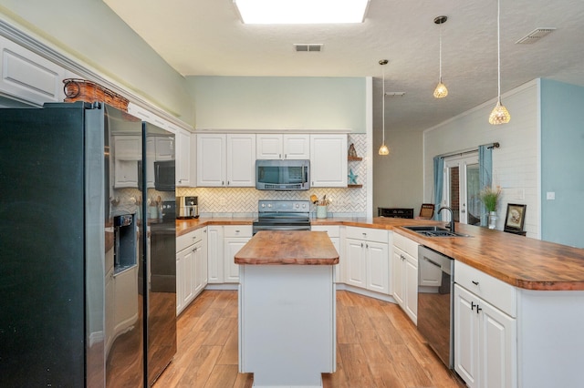 kitchen with kitchen peninsula, appliances with stainless steel finishes, a center island, white cabinetry, and butcher block counters