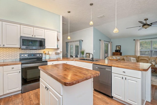 kitchen featuring kitchen peninsula, stainless steel appliances, white cabinets, butcher block countertops, and a kitchen island