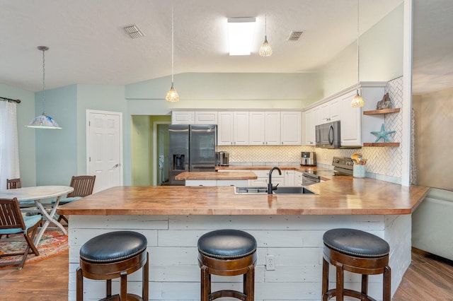 kitchen with a breakfast bar area, sink, wooden counters, and appliances with stainless steel finishes