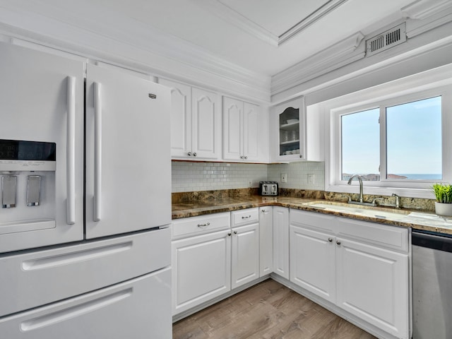 kitchen with dark stone countertops, white fridge with ice dispenser, dishwasher, and white cabinets