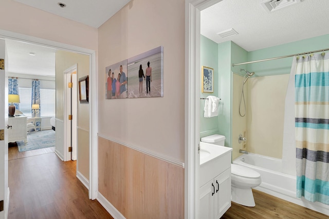 full bathroom with wood-type flooring, a textured ceiling, shower / bath combo with shower curtain, vanity, and toilet