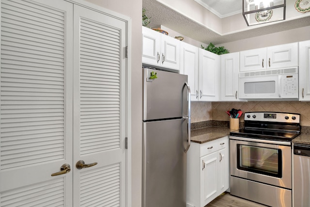 kitchen with dark stone counters, light hardwood / wood-style floors, white cabinetry, stainless steel appliances, and backsplash