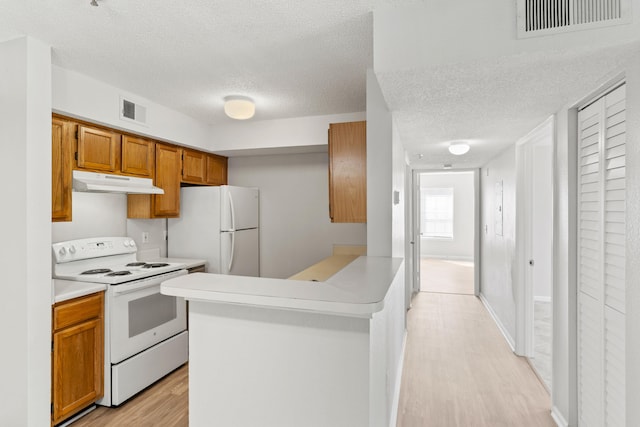 kitchen with a textured ceiling, light wood-type flooring, kitchen peninsula, and white appliances