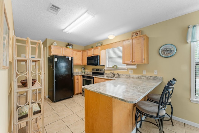 kitchen featuring light brown cabinets, light tile patterned floors, kitchen peninsula, a textured ceiling, and black appliances