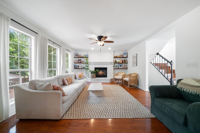 living room featuring dark hardwood / wood-style floors, ceiling fan, and a brick fireplace