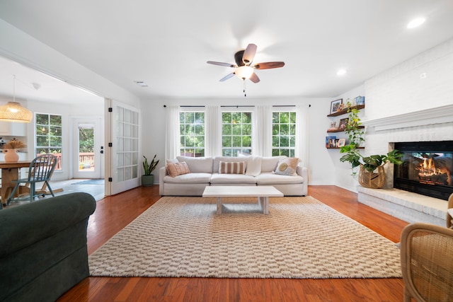 living room featuring a brick fireplace, ceiling fan, hardwood / wood-style floors, and a wealth of natural light