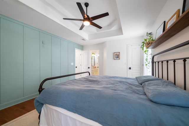 bedroom featuring connected bathroom, ceiling fan, a raised ceiling, and hardwood / wood-style flooring