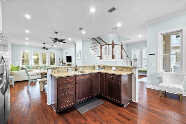 kitchen featuring light stone counters, ornamental molding, sink, dark hardwood / wood-style floors, and an island with sink