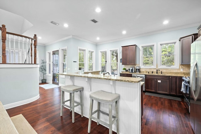 kitchen featuring dark hardwood / wood-style flooring, tasteful backsplash, light stone counters, crown molding, and an island with sink