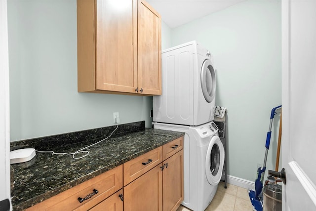 clothes washing area with cabinets, light tile patterned floors, and stacked washer and dryer