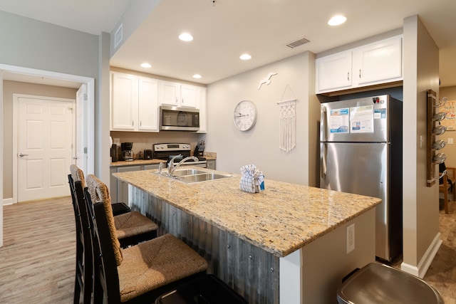 kitchen with white cabinets, a center island with sink, appliances with stainless steel finishes, and light stone countertops