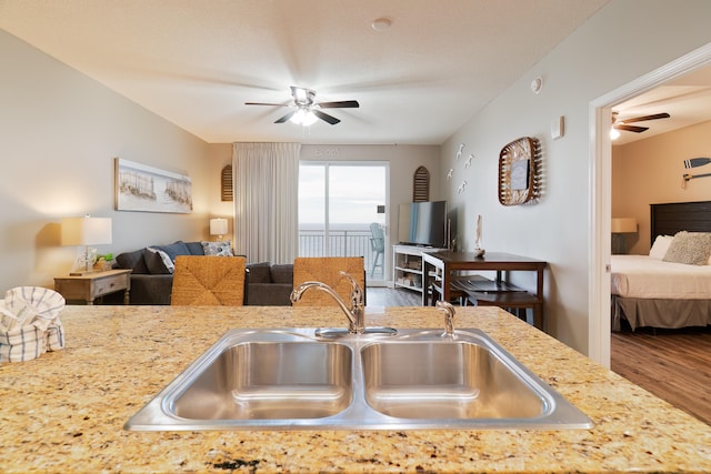 kitchen with wood-type flooring, light stone counters, ceiling fan, and sink