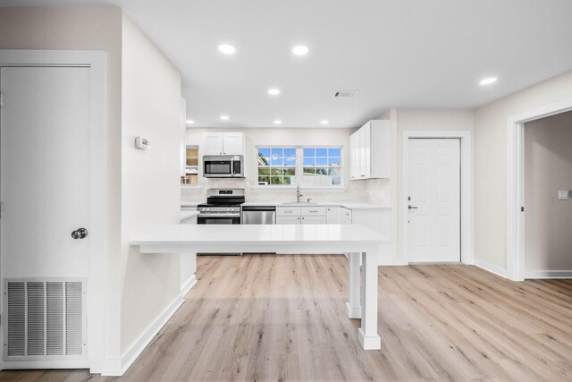 kitchen with appliances with stainless steel finishes, decorative backsplash, white cabinets, light wood-type flooring, and sink