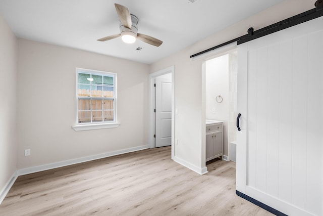 unfurnished bedroom with a barn door, ceiling fan, light hardwood / wood-style flooring, and ensuite bathroom