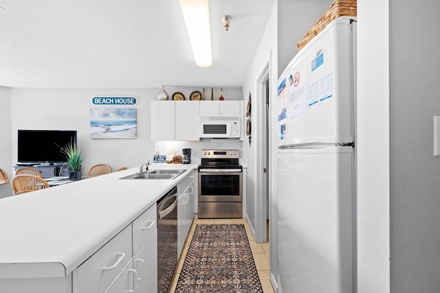 kitchen with stainless steel appliances, a sink, a peninsula, light countertops, and white cabinets