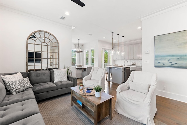 living room featuring sink, crown molding, dark hardwood / wood-style flooring, and an inviting chandelier