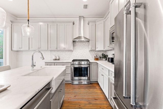 kitchen featuring wall chimney range hood, high quality appliances, sink, decorative light fixtures, and light wood-type flooring