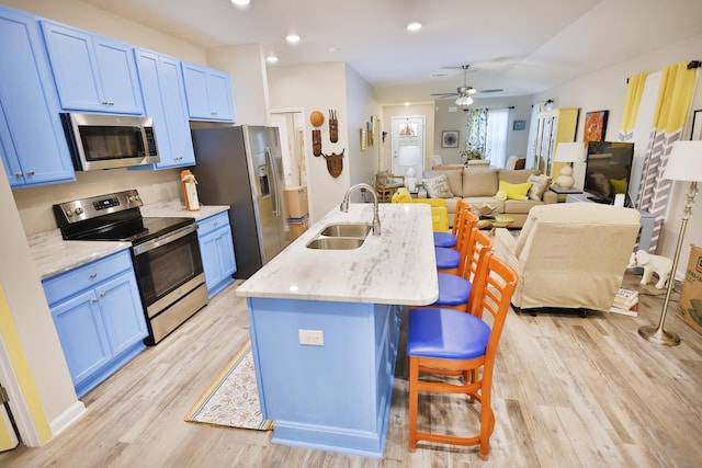 kitchen featuring blue cabinets, sink, a kitchen island with sink, appliances with stainless steel finishes, and a breakfast bar