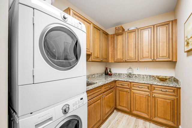 laundry area featuring light hardwood / wood-style flooring, cabinets, and stacked washer and clothes dryer