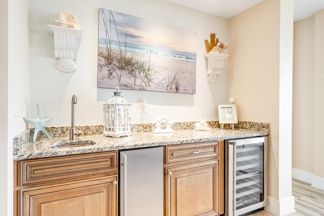 bar featuring stainless steel refrigerator, light stone countertops, sink, and beverage cooler