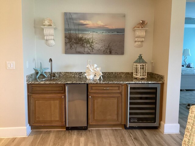 bar featuring dark stone countertops, stainless steel refrigerator, beverage cooler, and light hardwood / wood-style flooring