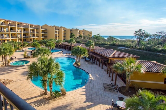 view of pool featuring a community hot tub, a water view, and a patio