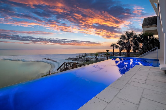 pool at dusk featuring a view of the beach and a water view