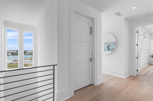 corridor with light wood finished floors, recessed lighting, a water view, visible vents, and baseboards