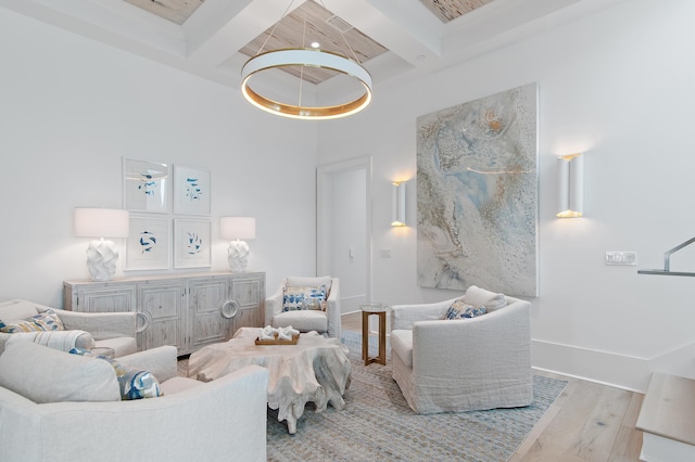 living room with beam ceiling, light wood finished floors, a towering ceiling, coffered ceiling, and baseboards