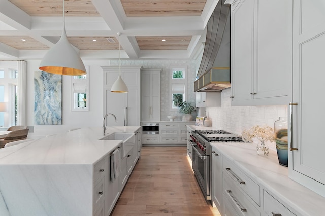 kitchen featuring decorative light fixtures, high end stainless steel range, a kitchen island with sink, custom exhaust hood, and a sink