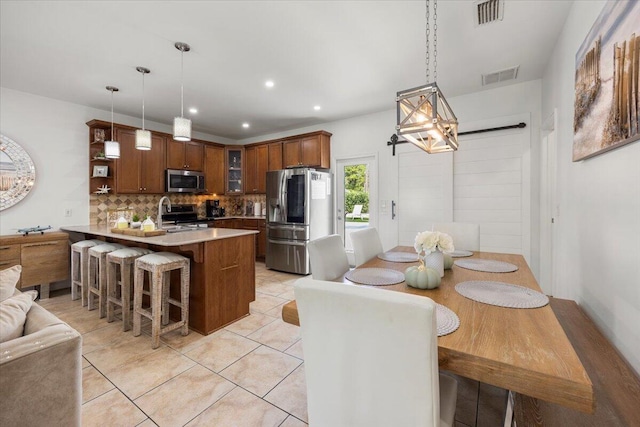 kitchen featuring tasteful backsplash, light tile patterned floors, stainless steel appliances, a kitchen bar, and decorative light fixtures