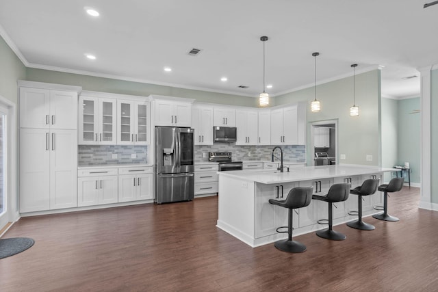 kitchen with appliances with stainless steel finishes, white cabinetry, pendant lighting, ornamental molding, and dark hardwood / wood-style floors