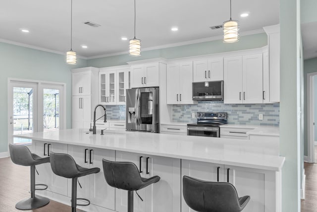 kitchen with hardwood / wood-style floors, appliances with stainless steel finishes, decorative light fixtures, and white cabinets