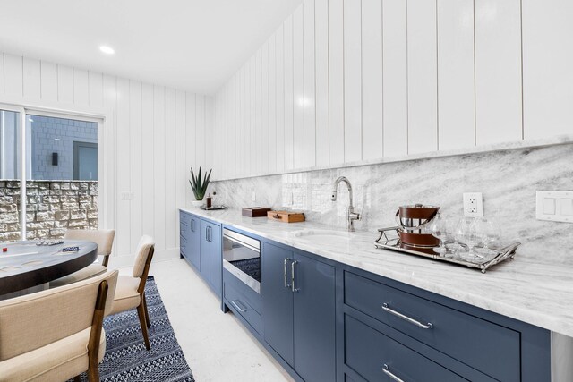 kitchen featuring light stone counters, wooden walls, backsplash, and sink