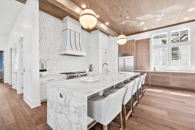 interior space featuring light hardwood / wood-style floors, a kitchen island with sink, white cabinets, stainless steel appliances, and decorative light fixtures