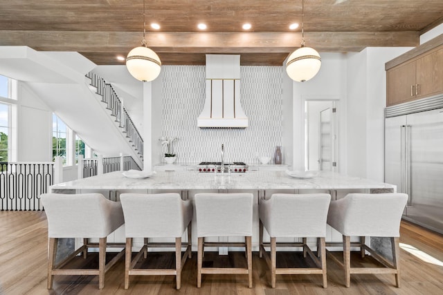 kitchen featuring light wood-type flooring, premium range hood, pendant lighting, and stainless steel built in fridge