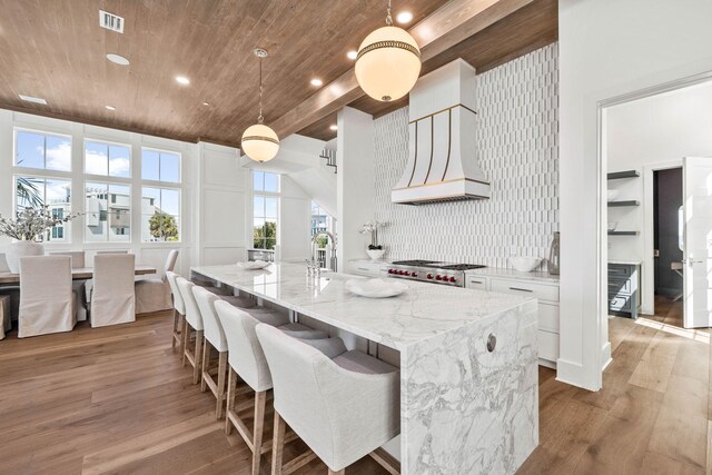 kitchen with light wood-type flooring, light stone counters, white cabinetry, decorative backsplash, and decorative light fixtures